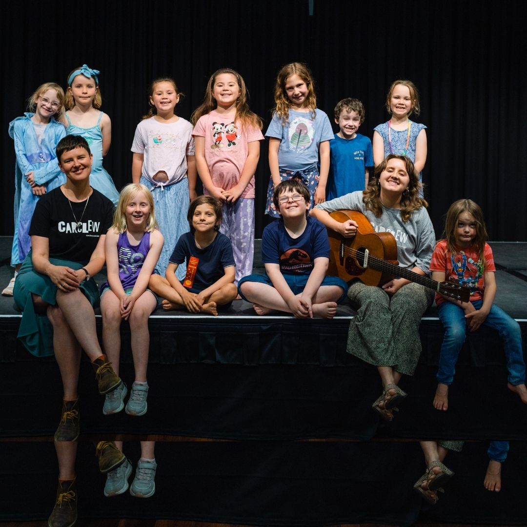 Children sitting on stage with stage sparks mentors Naomi Keyte and Kaite Pomery