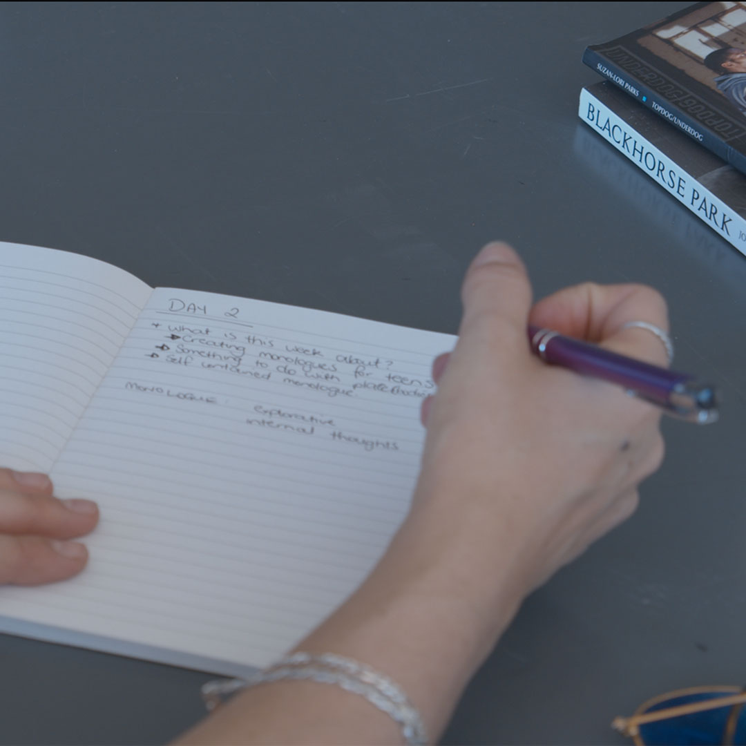 A hand holding a pen writing in a journal
