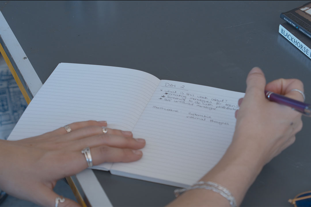 A hand holding a pen writing in a journal