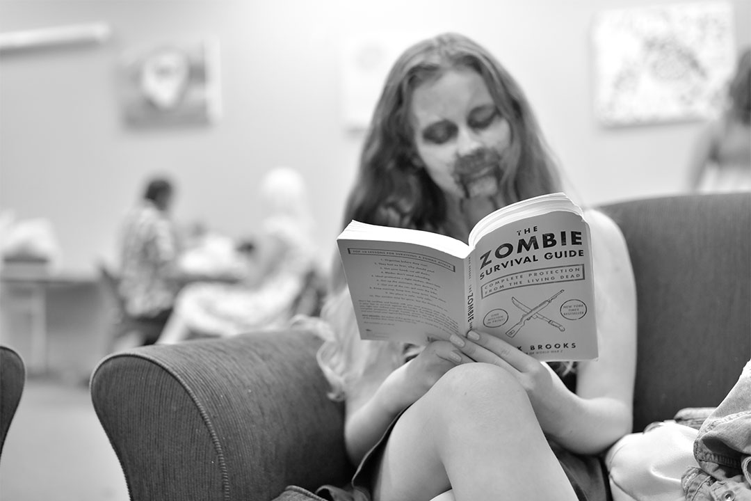 A female zombie reading "How to survive the zombie apocalypse"