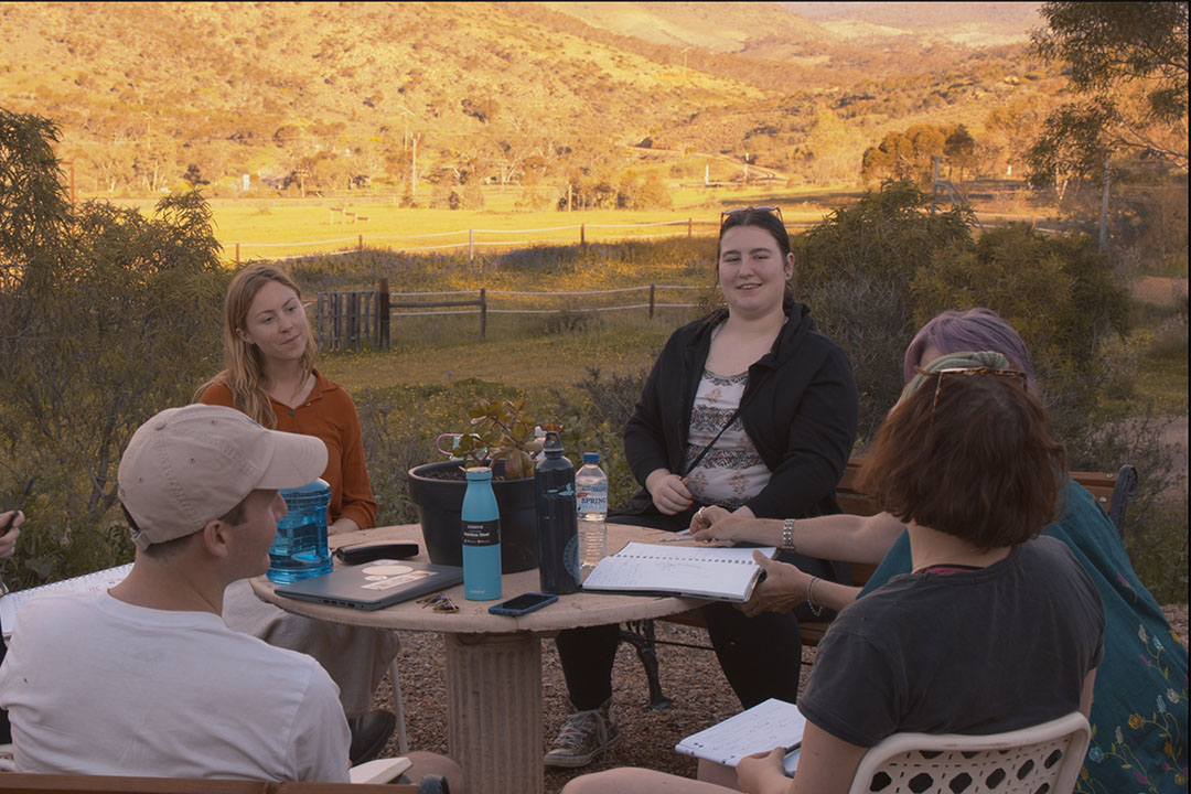 Four writers sit around a table in a valley at sunset